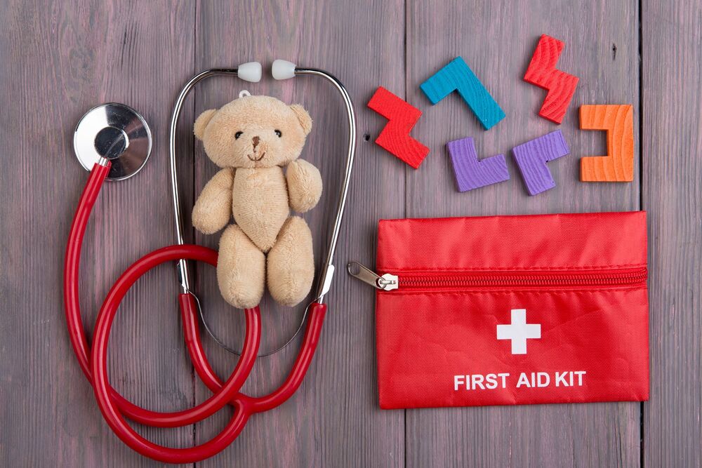Little toy bear, stethoscope and first aid kit on the wooden desk - children health care concept, pediatrist workplace